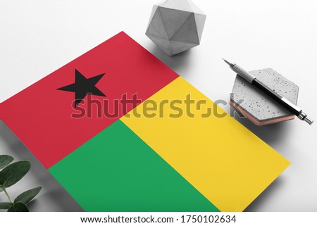 Guinea flag on minimalist paper background. National invitation letter with stylish pen on stone. Communication concept.