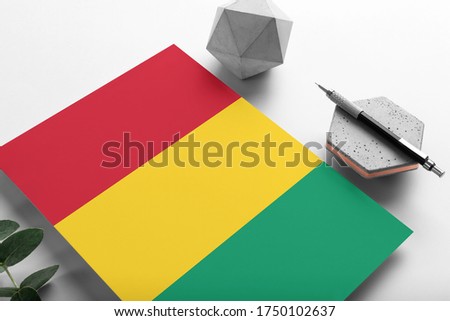 Guinea Bissau flag on minimalist paper background. National invitation letter with stylish pen on stone. Communication concept.