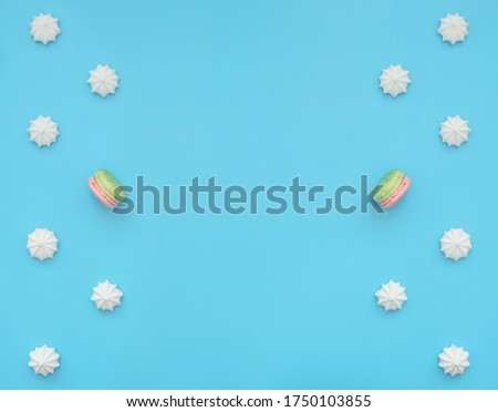 Delicious white merengues with one macarons among them on blue background. Happy day, breakfast, good morning concepts. Time for tea. Greeting or invitation card. Flat lay style with copy space.