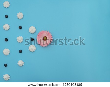 Delicious white merengues, fresh blueberries and a flower on blue background. Happy day, breakfast, good morning concepts. Time for tea. Greeting or invitation card. Flat lay style with copy space.