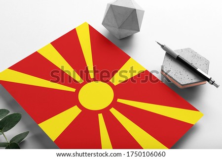 Macedonia flag on minimalist paper background. National invitation letter with stylish pen on stone. Communication concept.