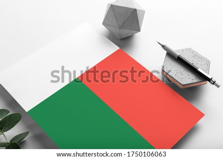 Madagascar flag on minimalist paper background. National invitation letter with stylish pen on stone. Communication concept.