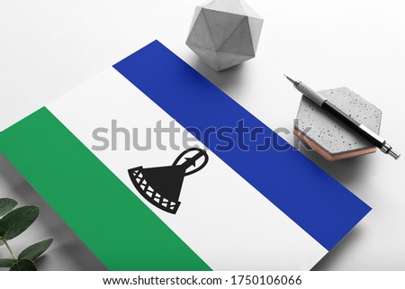 Lesotho flag on minimalist paper background. National invitation letter with stylish pen on stone. Communication concept.