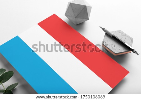 Luxembourg flag on minimalist paper background. National invitation letter with stylish pen on stone. Communication concept.