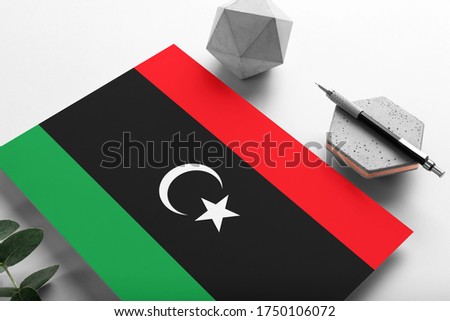 Libya flag on minimalist paper background. National invitation letter with stylish pen on stone. Communication concept.