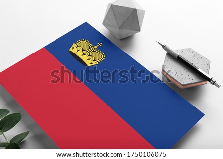 Liechtenstein flag on minimalist paper background. National invitation letter with stylish pen on stone. Communication concept.