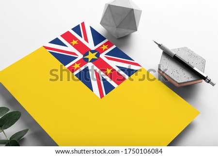 Niue flag on minimalist paper background. National invitation letter with stylish pen on stone. Communication concept.