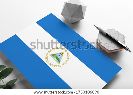 Nicaragua flag on minimalist paper background. National invitation letter with stylish pen on stone. Communication concept.