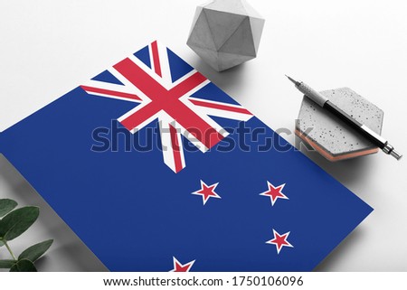 New Zealand flag on minimalist paper background. National invitation letter with stylish pen on stone. Communication concept.