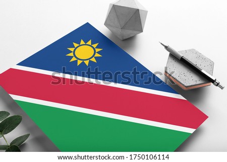 Namibia flag on minimalist paper background. National invitation letter with stylish pen on stone. Communication concept.