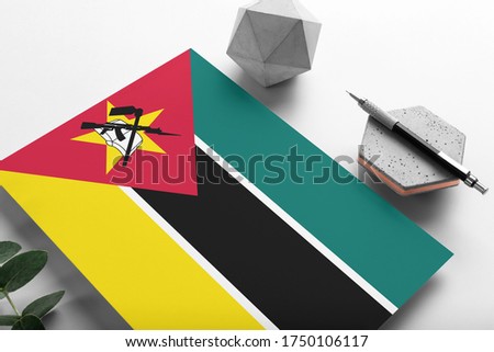 Mozambique flag on minimalist paper background. National invitation letter with stylish pen on stone. Communication concept.
