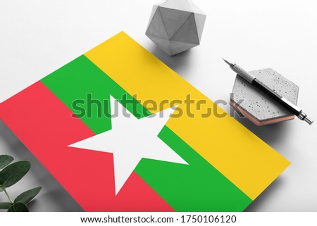 Myanmar flag on minimalist paper background. National invitation letter with stylish pen on stone. Communication concept.