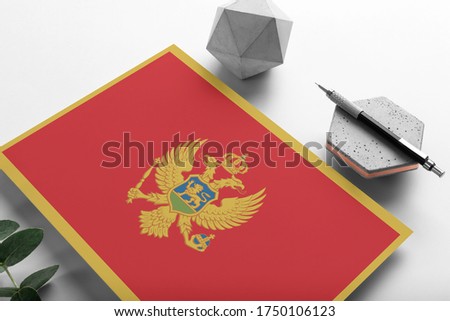 Montenegro flag on minimalist paper background. National invitation letter with stylish pen on stone. Communication concept.