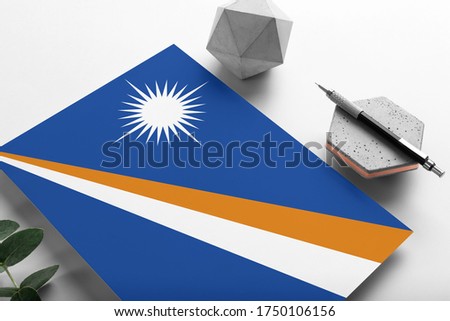 Marshall Islands flag on minimalist paper background. National invitation letter with stylish pen on stone. Communication concept.