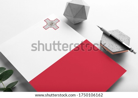 Malta flag on minimalist paper background. National invitation letter with stylish pen on stone. Communication concept.