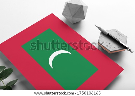 Maldives flag on minimalist paper background. National invitation letter with stylish pen on stone. Communication concept.