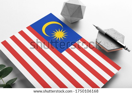 Malaysia flag on minimalist paper background. National invitation letter with stylish pen on stone. Communication concept.