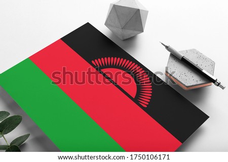 Malawi flag on minimalist paper background. National invitation letter with stylish pen on stone. Communication concept.