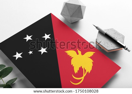 Papua New Guinea flag on minimalist paper background. National invitation letter with stylish pen on stone. Communication concept.