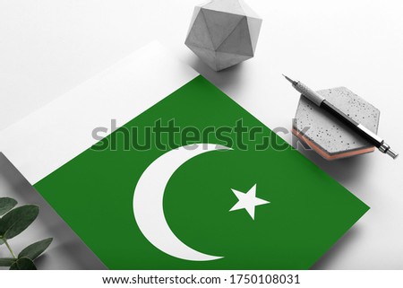 Pakistan flag on minimalist paper background. National invitation letter with stylish pen on stone. Communication concept.