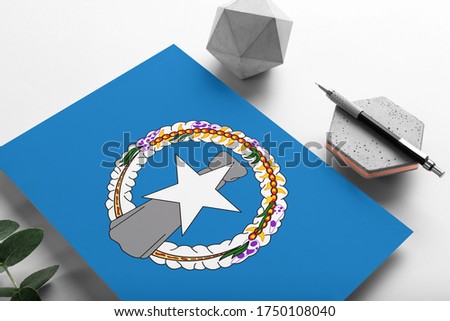 Northern Mariana Islands flag on minimalist paper background. National invitation letter with stylish pen on stone. Communication concept.