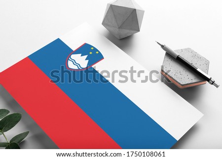 Slovenia flag on minimalist paper background. National invitation letter with stylish pen on stone. Communication concept.