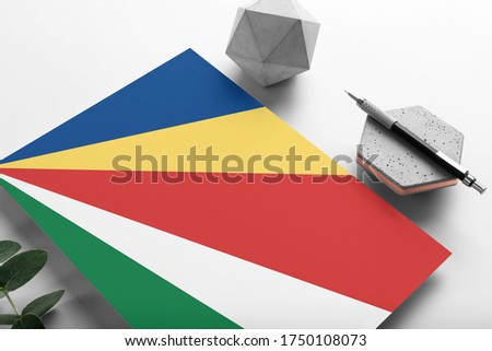 Seychelles flag on minimalist paper background. National invitation letter with stylish pen on stone. Communication concept.