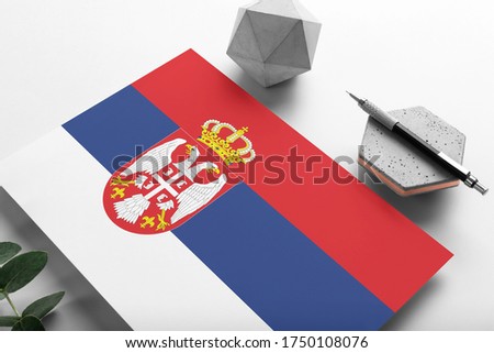 Serbia flag on minimalist paper background. National invitation letter with stylish pen on stone. Communication concept.