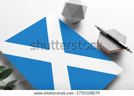 Scotland flag on minimalist paper background. National invitation letter with stylish pen on stone. Communication concept.