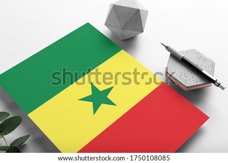 Senegal flag on minimalist paper background. National invitation letter with stylish pen on stone. Communication concept.