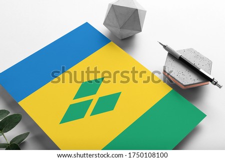 Saint Vincent And The Grenadines flag on minimalist paper background. National invitation letter with stylish pen on stone. Communication concept.