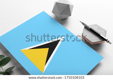 Saint Lucia flag on minimalist paper background. National invitation letter with stylish pen on stone. Communication concept.