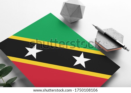 Saint Kitts And Nevis flag on minimalist paper background. National invitation letter with stylish pen on stone. Communication concept.