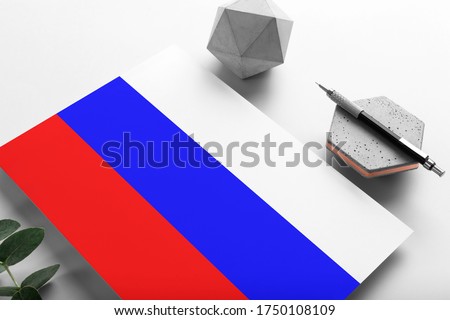 Russia flag on minimalist paper background. National invitation letter with stylish pen on stone. Communication concept.