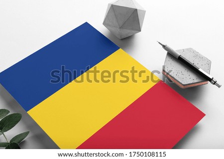 Romania flag on minimalist paper background. National invitation letter with stylish pen on stone. Communication concept.