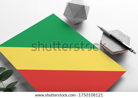 Republic Of The Congo flag on minimalist paper background. National invitation letter with stylish pen on stone. Communication concept.