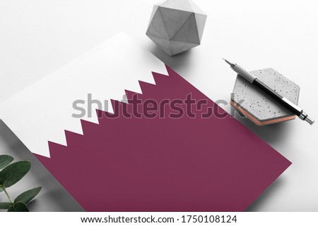 Qatar flag on minimalist paper background. National invitation letter with stylish pen on stone. Communication concept.
