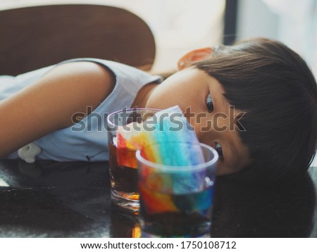Selective focus of young little girl lying head down on the table watching paper dissolving and water in the glasses change color for rainbow growing experiment. Education concept.