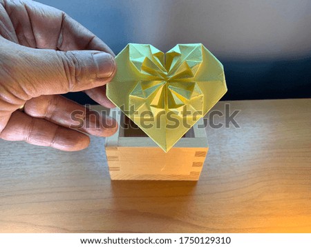 Hand putting a paper heart into a wooden box. The way of taking care of someone or customer service concept.