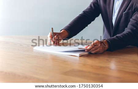 business man wear  black suit use pen to signing contract documents on a wooden desk in the office