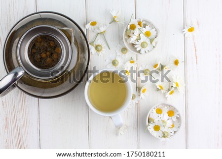 Cup of chamomile tea with flowers on white wooden background