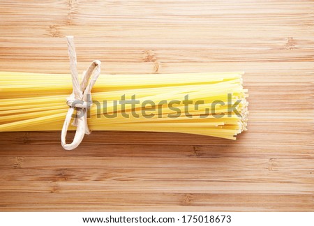Bundle of Italian spaghetti pasta tied with string lying on old textured wooden boards with a scattering of flour