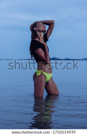Fit tanned young caucasian Woman in sea at sunset, dark light. Female in black top and yellow panties on tropical beach. Weight loss motivation, slim body.