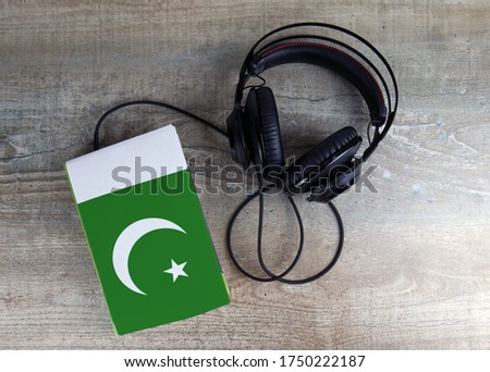 Headphones and book. The book has a cover in the form of Pakistan flag. Concept audiobooks. Learning languages.