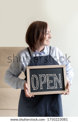 Woman's Hands Holds Dashboard with Text Open. Middle Aged 50 Plus Lady in Apron Shows Opening of the Cafe or Market.