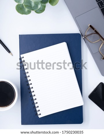 White office desk table with blank notebook, notebook, laptop compute, glasses, cup of black coffee and supplies. Top view with copy space, flat lay.