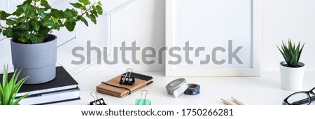 Desk with office supplies and a white frame mockup. Blank wall copy space. Panorama