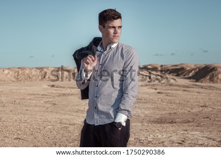 portrait of a man in the desert, in a shirt holding a black jacket over his shoulder