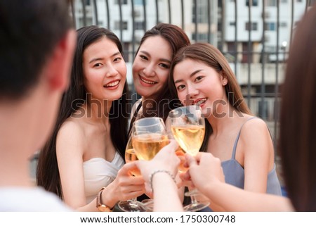 Group of young Asian friends are toasting or cheering and hanging out together at rooftop party.
