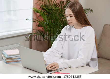 Beautiful young girl sitting in the living room at the table with a laptop.